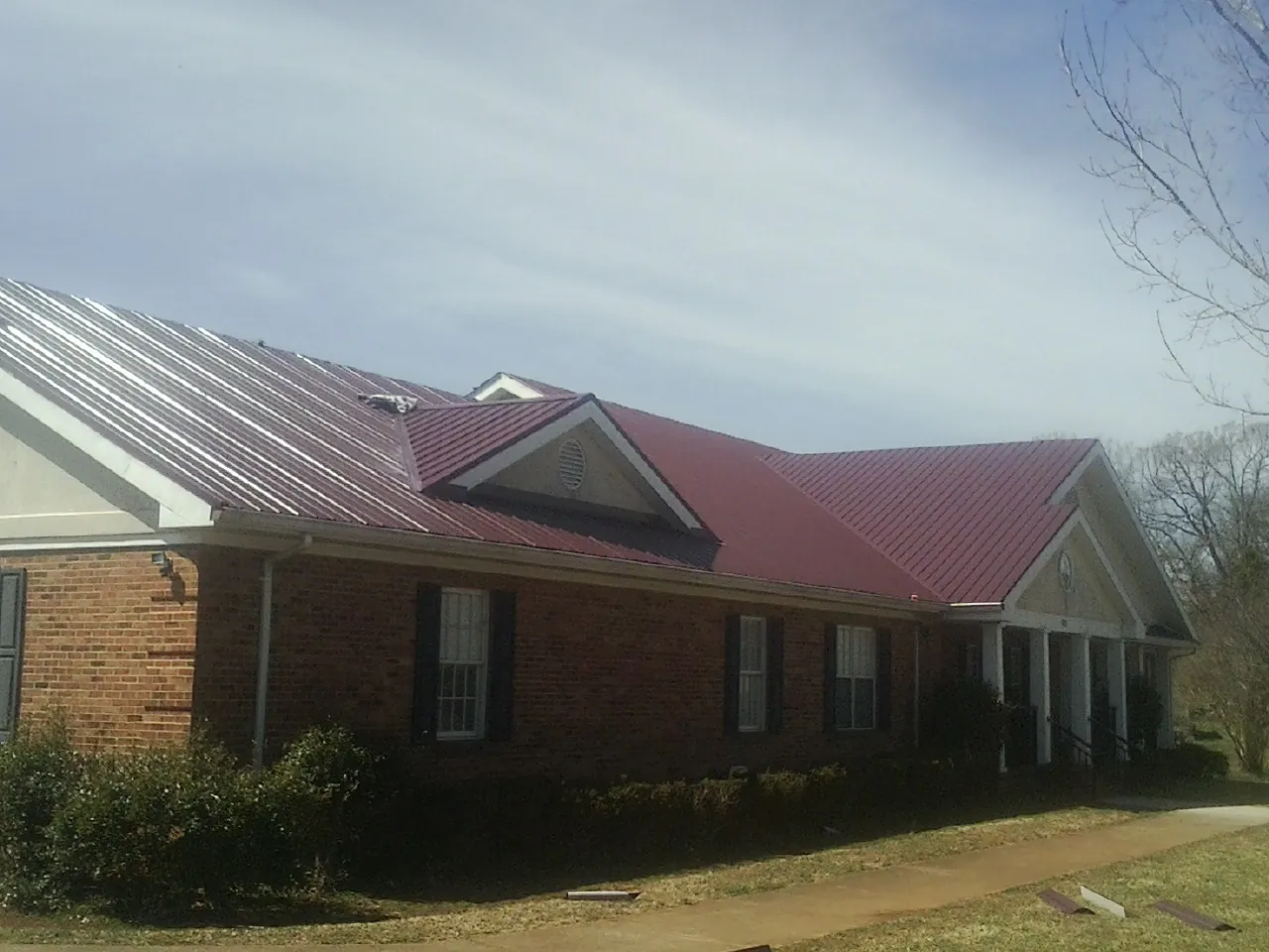 Red metal roof with gabled entries on a long brick building, from a Hail Damage Roof Repair job in Middleton