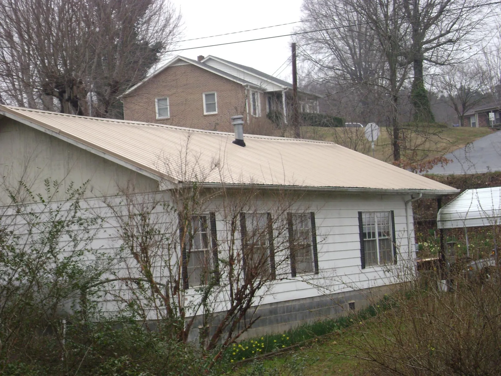 Tan metal roof on a white sided house set into a hillside — Commercial Roofing by Roofing Brothers in Middleton